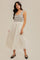 woman wearing a striped sleeveless midi dress with a fitted bodice and a flowing white skirt, paired with black flats