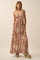 woman wearing a brown floral maxi dress with a deep v-neck and side slits, standing with hands in pockets