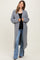 woman wearing a gray long cardigan over a black top and flared jeans, showcasing a baby bump