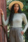 woman wearing a light gray long sleeve top and matching drawstring pants, standing outdoors with a wide-brimmed hat