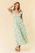 woman wearing a maxi dress with a square neckline, green floral print, and ruffled straps on a beige background