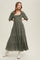 woman wearing an olive green tiered maxi dress with puff sleeves and ruffle detailing, posing in white boots