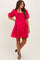 woman wearing a bright pink maternity dress with puff sleeves and a smocked bodice, standing and smiling