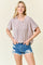 woman wearing a light beige striped oversized t-shirt and distressed denim shorts, smiling toward the camera