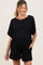 woman wearing a black short sleeve maternity top and matching shorts with a waist tie detail, smiling