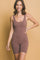 woman wearing a mauve ribbed sleeveless jumpsuit with shorts, smiling against a light yellow background