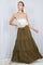 woman wearing a light gold sleeveless top and an olive green tiered maxi skirt, posing against a draped background