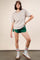 woman wearing a beige oversized t-shirt with a pocket, green athletic shorts, and sneakers with striped socks
