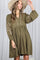 woman wearing a green long sleeve dress with embroidered details and a buttoned front, holding a wide-brimmed hat
