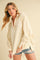 woman wearing a light beige oversized pullover sweatshirt with button detailing and rolled sleeves, paired with distressed denim shorts