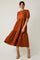 woman wearing an orange puff sleeve midi dress with a tiered skirt and floral texture, posing against a neutral background
