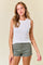 woman wearing a white ribbed tank top and green shorts with a casual stance and soft smile