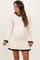 woman wearing a cream ribbed maternity dress with black trim at the neckline and hem, showing her baby bump
