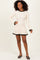 woman wearing a cream ribbed long sleeve dress with black ruffles at the neckline and hem, standing and smiling