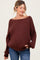 woman wearing a burgundy oversized ribbed maternity sweater and blue jeans, showcasing her baby bump