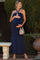 woman wearing a navy blue strapless maternity maxi dress and holding her baby bump, styled with a silver bag and accessories