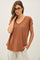 woman wearing a rust-colored short sleeve top with a v-neck and relaxed fit, styled with light beige trousers