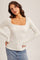 woman wearing a cream long sleeve ribbed top with a square neckline and lace detailing, paired with a denim skirt