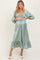 woman wearing a light green maternity dress with a smocked bodice and ruffled hem, holding her baby bump