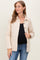 woman wearing a cream quilted maternity jacket over a black top, smiling and standing against a light background