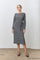 woman wearing a gray striped long sleeve dress with a Tie waist detail, standing against a white wall
