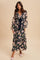 woman wearing a black floral maxi dress with long sleeves and a tie waist, standing on a neutral background