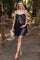 woman wearing a black sequin maternity dress with a bow detail and holding a clutch, baby bump visible
