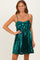 woman wearing a sparkly emerald green sequin dress with a bow detail and adjustable straps
