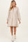 woman wearing a beige floral maternity dress with long sleeves and pom-pom trim, showcasing her baby bump
