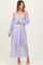 woman wearing a lavender off-the-shoulder maternity dress with long sheer sleeves and a fitted bodice, cradling her baby bump