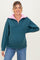 woman wearing a teal maternity pullover with a pink collar and a zipper, showing her baby bump