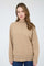 woman wearing a beige oversized sweater with a high neck and long sleeves, paired with blue jeans