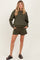 woman wearing an olive green maternity sweatshirt and matching shorts, with pockets, styled casually