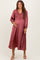 woman wearing a dusty rose long sleeve maternity dress with a smocked bodice and pleated skirt, holding her baby bump