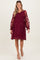 woman wearing a burgundy maternity dress with floral lace overlay and long sleeves, smiling with a baby bump visible