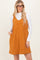 woman wearing an orange corduroy sleeveless dress with pockets over a white long sleeve top
