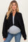 woman wearing a black cropped maternity cardigan over a light gray top and showing her baby bump with jeans