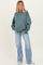 woman wearing a green oversized sweatshirt and light blue flared jeans, showcasing a casual maternity outfit