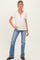 woman wearing a cream maternity top with a v-neck and button details, paired with blue flared jeans and showing her baby bump
