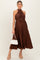 woman wearing a brown pleated maternity dress with a halter neck and a tie at the waist, holding a white handbag