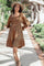 woman wearing a brown smocked dress with long sleeves and a tiered hem, styled with a wide-brimmed hat