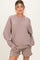woman wearing a taupe oversized maternity sweatshirt and matching shorts, posing with hands in pockets