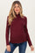 woman wearing a burgundy ribbed maternity top with a ruffled neckline and a visible baby bump