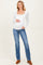 woman wearing a white long sleeve maternity top and blue flared jeans, holding her baby bump
