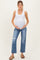 woman wearing a white tank top and blue distressed maternity jeans, holding her baby bump