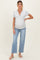 woman wearing a light gray maternity henley top with a button detail and blue maternity jeans, showing her baby bump