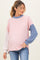 woman wearing a color-blocked pink and blue maternity top with ribbed texture and long sleeves, gently cradling her baby bump