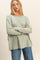 woman wearing a light green long sleeve top with a relaxed fit and paired with blue jeans