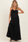 woman wearing a black maternity maxi dress with a tie detail at the bust and a side slit, showing off her baby bump