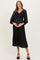 woman wearing a black pleated maternity dress with a smocked bodice and balloon sleeves, holding her baby bump